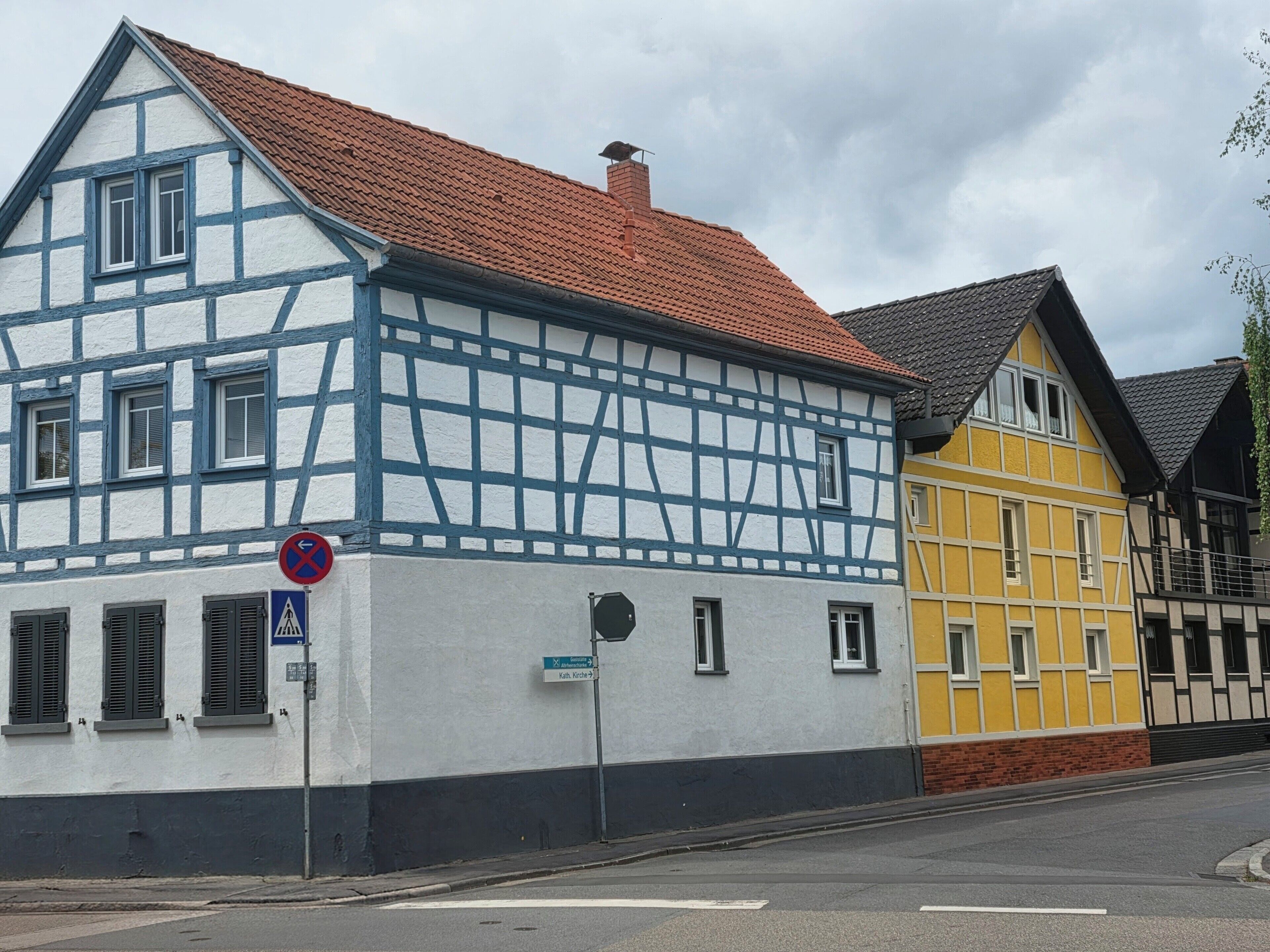 A traditional half-timbered building with a red-tiled roof, a blue and white facade, and a street sign indicating a no parking zone.