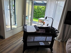 Una habitación con un gran ventanal corredero que da a un patio, un cochecito de bebé negro, un escritorio blanco y un televisor montado en la pared.