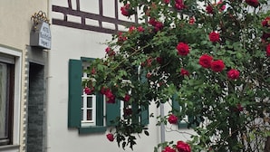 A traditional half-timbered building with green shutters, a visible hotel sign, and a rose bush in the foreground. - All-In Rhein-Main - Pool, Hot Tub, Sauna, Fitness Center & Workspace! (Ginsheim-Gustavsburg)