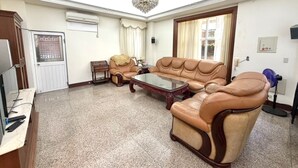 A living room with a sofa, armchairs, a glass coffee table, a chandelier, a television, and a door with a window. - HeartBnb Villa (Taitung)