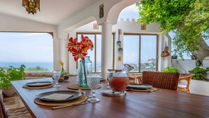 Taula de menjador preparada amb plats, gots i un ram de flors, amb vista a un paisatge idíl·lic.
