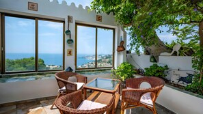 Un balcon doté de meubles en osier, de grandes fenêtres et offrant une vue sur la mer.