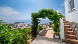 Escales que condueixen a un edifici blanc amb vistes al mar i un jardí amb un arc de gespa.