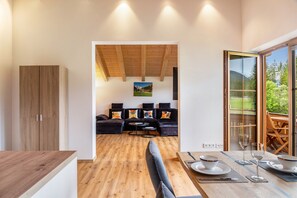 Un interior moderno con techo de madera, una zona de comedor con mesa dispuesta para dos personas, y un sofá al fondo.