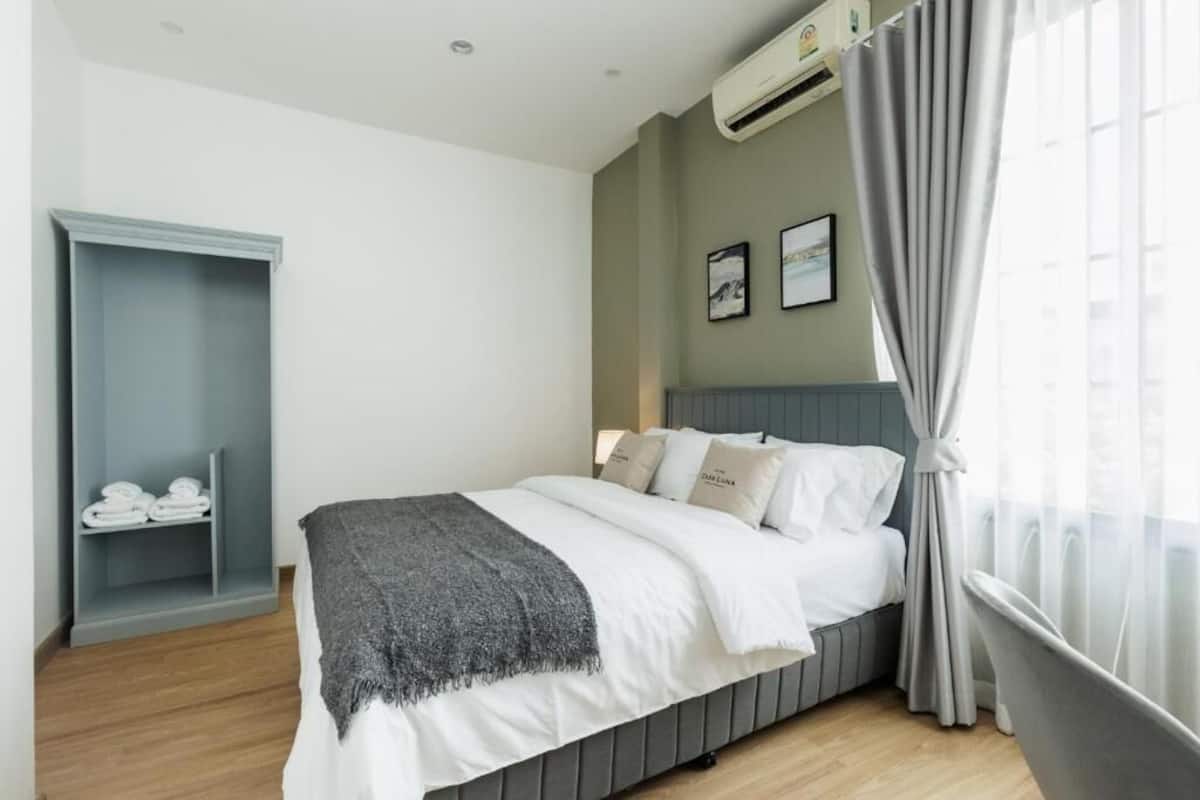 A bedroom with a bed, a grey wardrobe, a grey chair, and a window with curtains.
