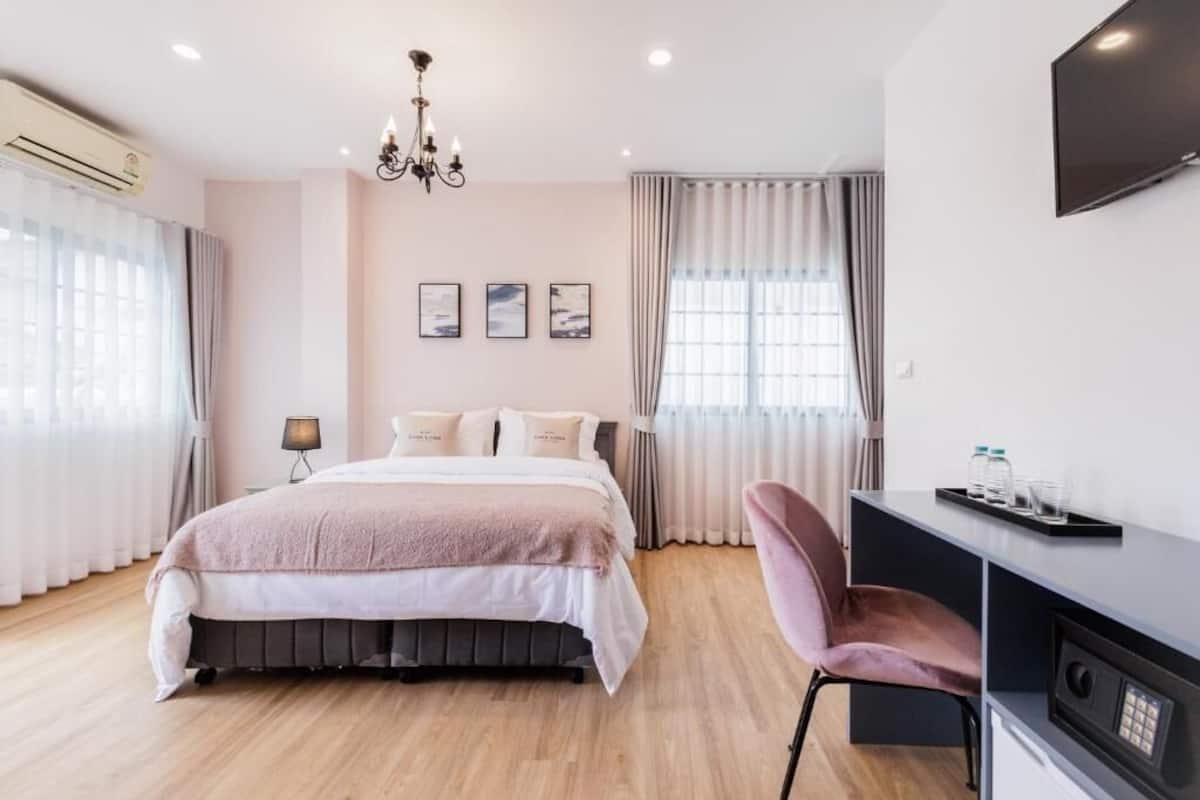 A modern bedroom with a bed, a desk, a chair, a TV, and a window with curtains.