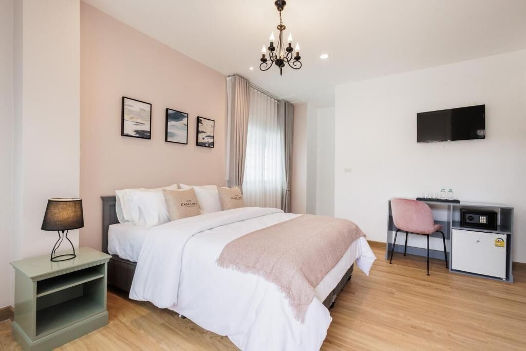 Un dormitorio con cama, mesita de noche, escritorio, silla, televisor y cortinas.