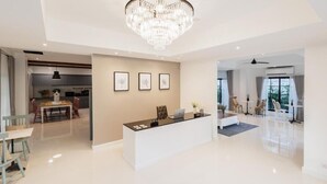 Ampla sala de estar com uma receção central, um candelabro e uma área de refeições visível ao fundo.