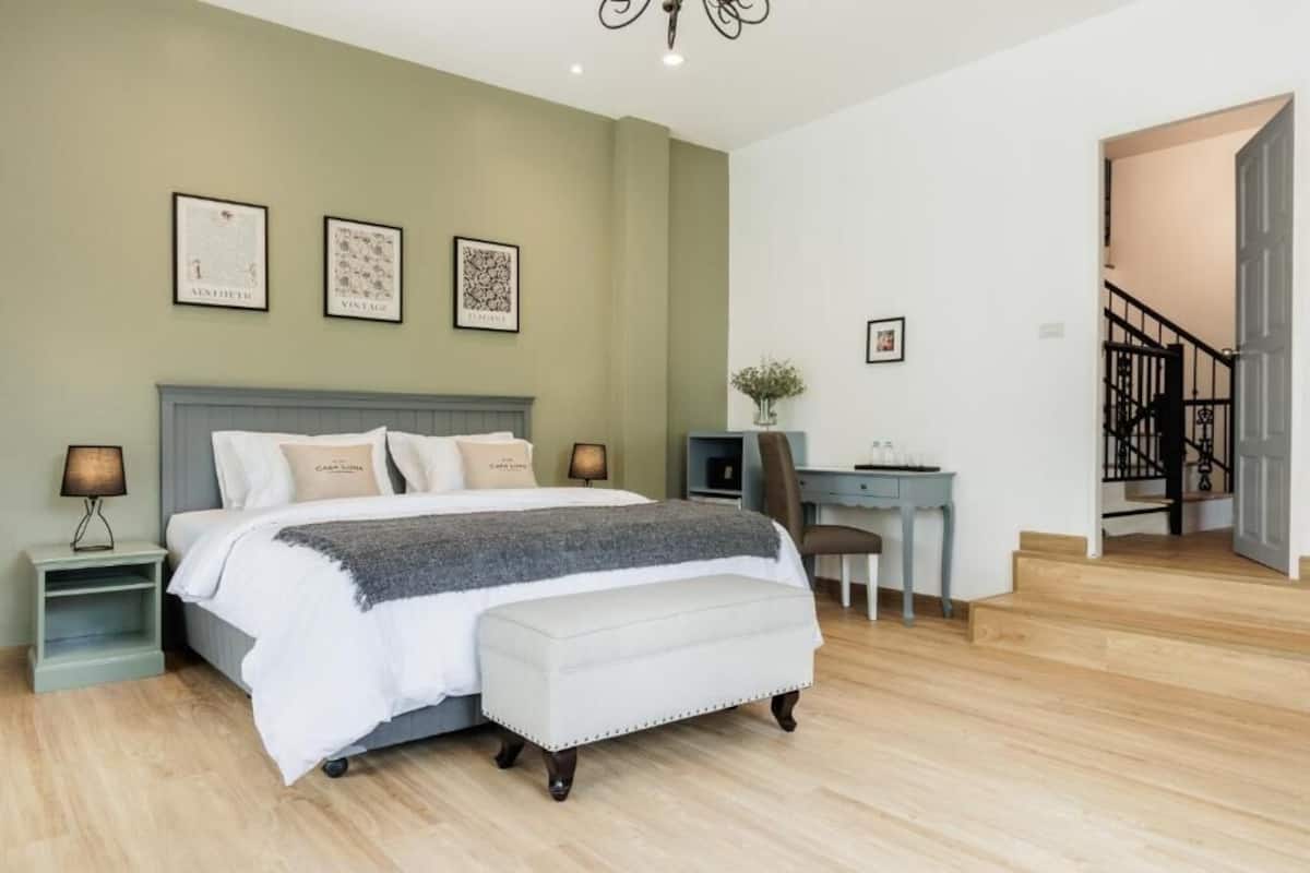 A bedroom with a bed, bedside tables, a desk, and a staircase.