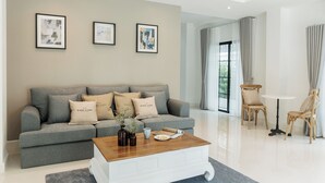 Uma sala de estar moderna com um sofá cinza, uma mesa de centro e um espaço de refeições com mesa e cadeiras.