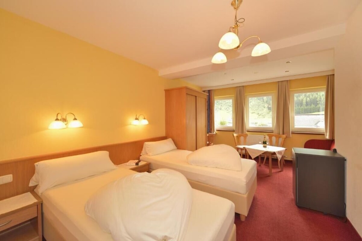 A hotel room with two beds, a desk, a chair, and a dining table.