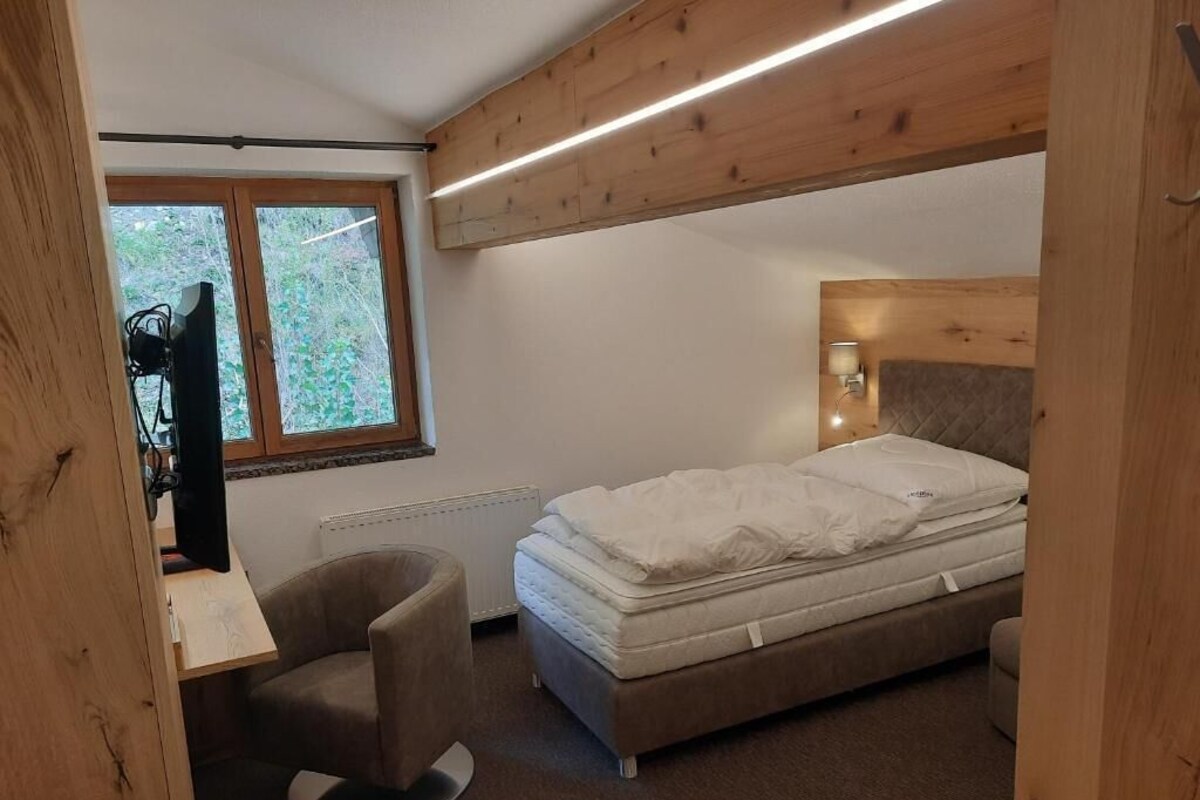 A bedroom with a bed, a desk, a chair, a window, and a wooden ceiling.