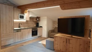 A modern kitchen with wooden cabinets, a microwave, and a large flat-screen TV. - Viktoria (Sankt Anton am Arlberg)