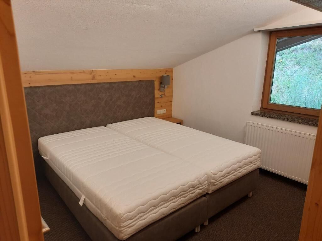 A bedroom with a bed, wooden headboard, a window with a view, and a radiator.