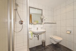 A bathroom with a shower, sink, toilet, and a mirror with a checkered frame.