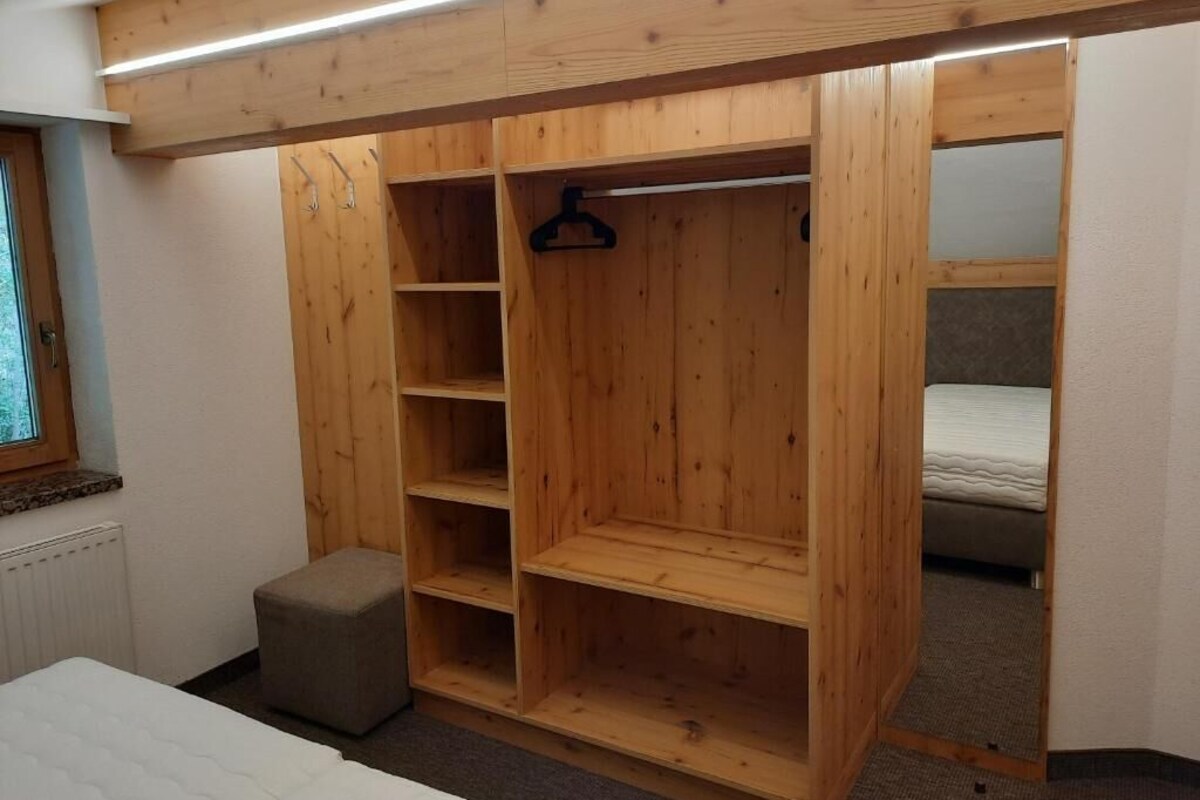 A bedroom with a wooden wardrobe, a bed, and a small stool.