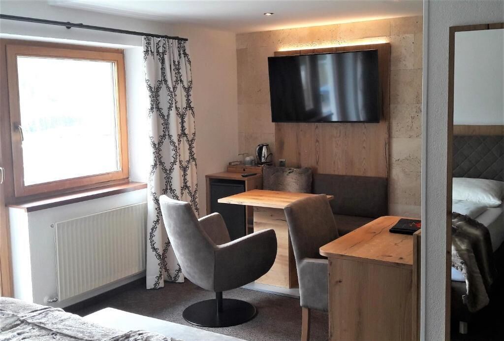 A hotel room with a bed, a desk with a chair, a television mounted on the wall, a window with curtains, and a radiator.