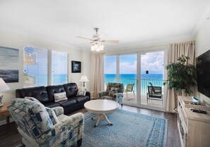 Ein Wohnzimmer mit einem schwarzen Ledersofa, gemusterten Sesseln, einem runden Couchtisch und Meerblick durch große Fenster.