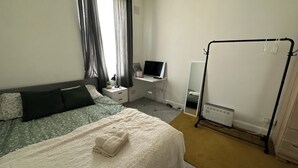 A bedroom with a bed, bedside table, TV, and a radiator. - Modern studio in heart of KingsX Eurostar (London)