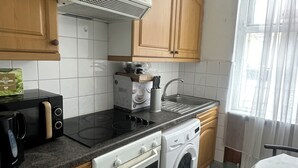 A kitchen with wooden cabinets, a stove, a microwave, a sink, and a washing machine.