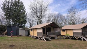 A campsite with two tents, a small shed, and a tree with pink flowers. - The Safari Lodge Tent We offer you unusual accommodation (Souleuvre en Bocage)