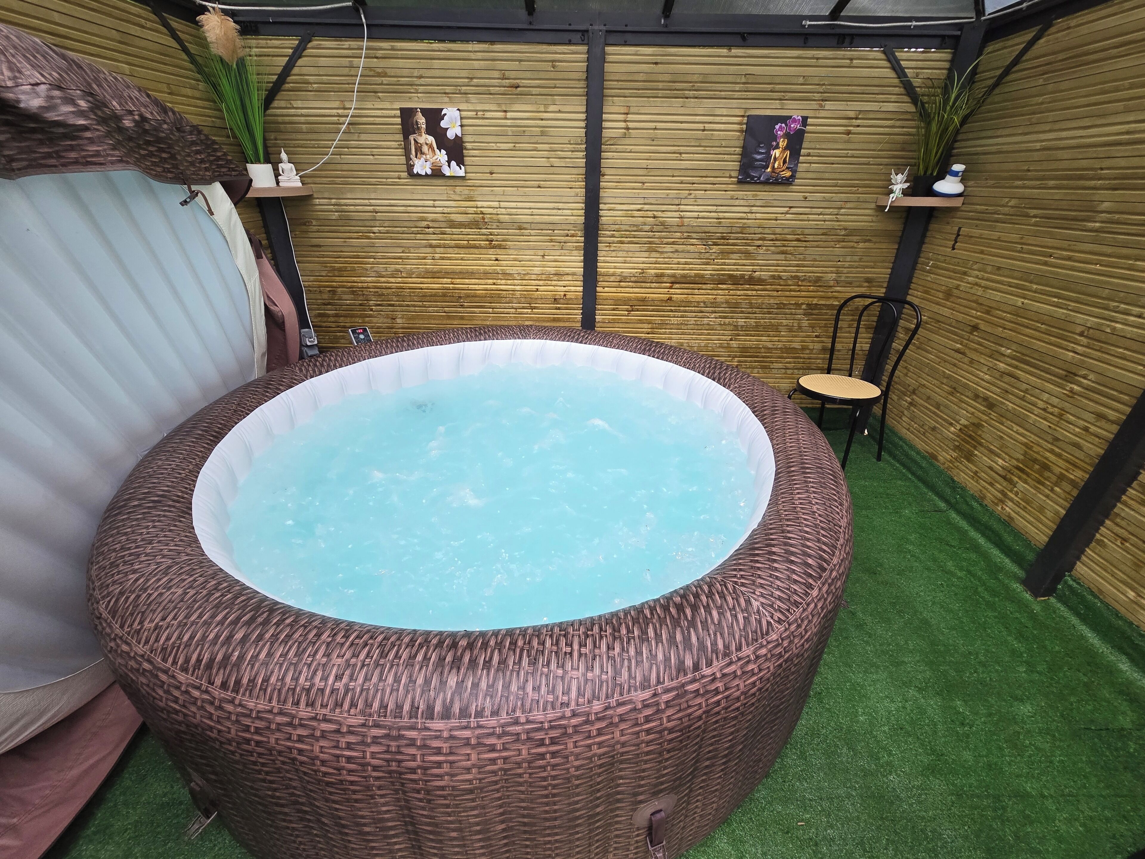 Un jacuzzi con revestimiento de mimbre, rodeado por un muro de madera y césped artificial.