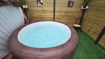 Un jacuzzi con revestimiento de mimbre, rodeado por un muro de madera y césped artificial.