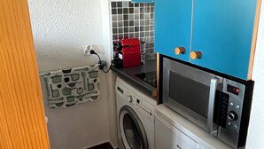A compact kitchen with a washing machine, a microwave, and a red appliance on the counter. - Charming 2-room apartment with magnificent sea view (Grosseto-Prugna)