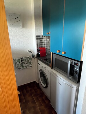 Eine kleine Küche mit Waschmaschine, Mikrowelle und einem roten Gerät auf der Arbeitsfläche.
