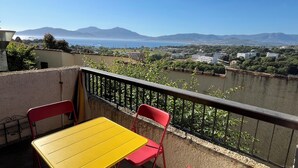 A balcony with a yellow table and red chairs, overlooking a river and distant mountains. - Charming 2-room apartment with magnificent sea view (Grosseto-Prugna)