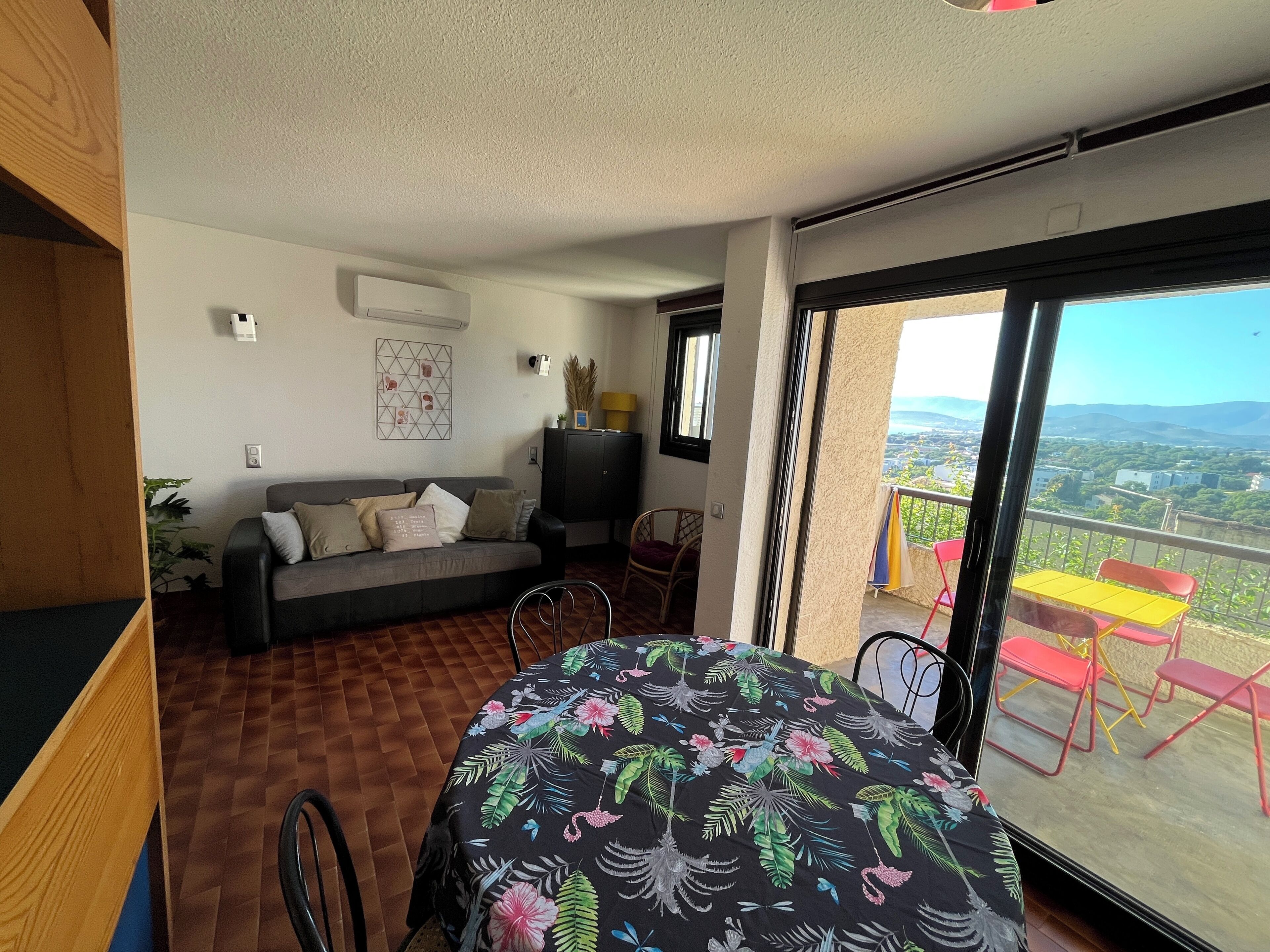 Una stanza con divano, un tavolo da pranzo con sedie, un balcone con vista e una finestra.
