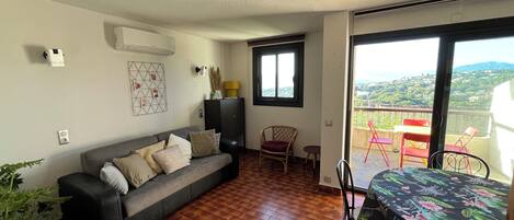 Olohuone, jossa on sohva, ruokapöytä tuoleineen, ikkuna ja näkymä ulos.