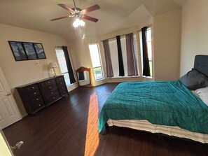 Ein Schlafzimmer mit Bett, Kommode, Deckenventilator und großen Fenstern.