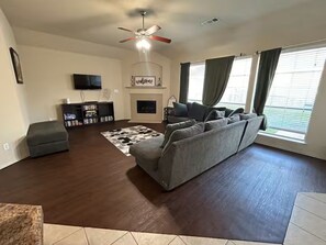 Ein Wohnzimmer mit Sofa, Hocker, Fernseher, Kamin und Deckenventilator.