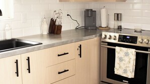 Eine moderne Küche mit hellen Holzschränken, einem Edelstahlherd, einer Kaffeemaschine und einem gemusterten Teppich.