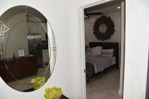 Ein Schlafzimmer mit einem Bett, einem großen Spiegel und Blick zur Küche.