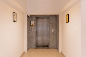 An elevator in a hallway with a tiled floor and plain walls. - Itsy Hotels Cozy Retreat - Near Mysore Palace & Zoo (Mysore)