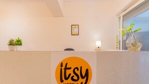 A reception desk with a logo, a potted plant, a framed certificate, and a window with a view. - Itsy Hotels Cozy Retreat - Near Mysore Palace & Zoo (Mysore)