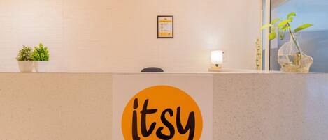 A reception desk with a logo, a potted plant, a framed certificate, and a window with a view.