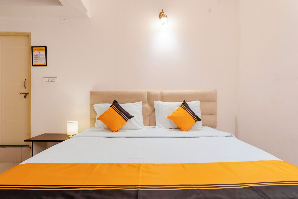 Habitación de hotel con una cama, dos almohadas, una mesita de noche, una lámpara y un aplique de pared.