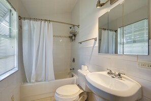 Et badeværelse med badekar, toilet, vask og bruseforhæng.