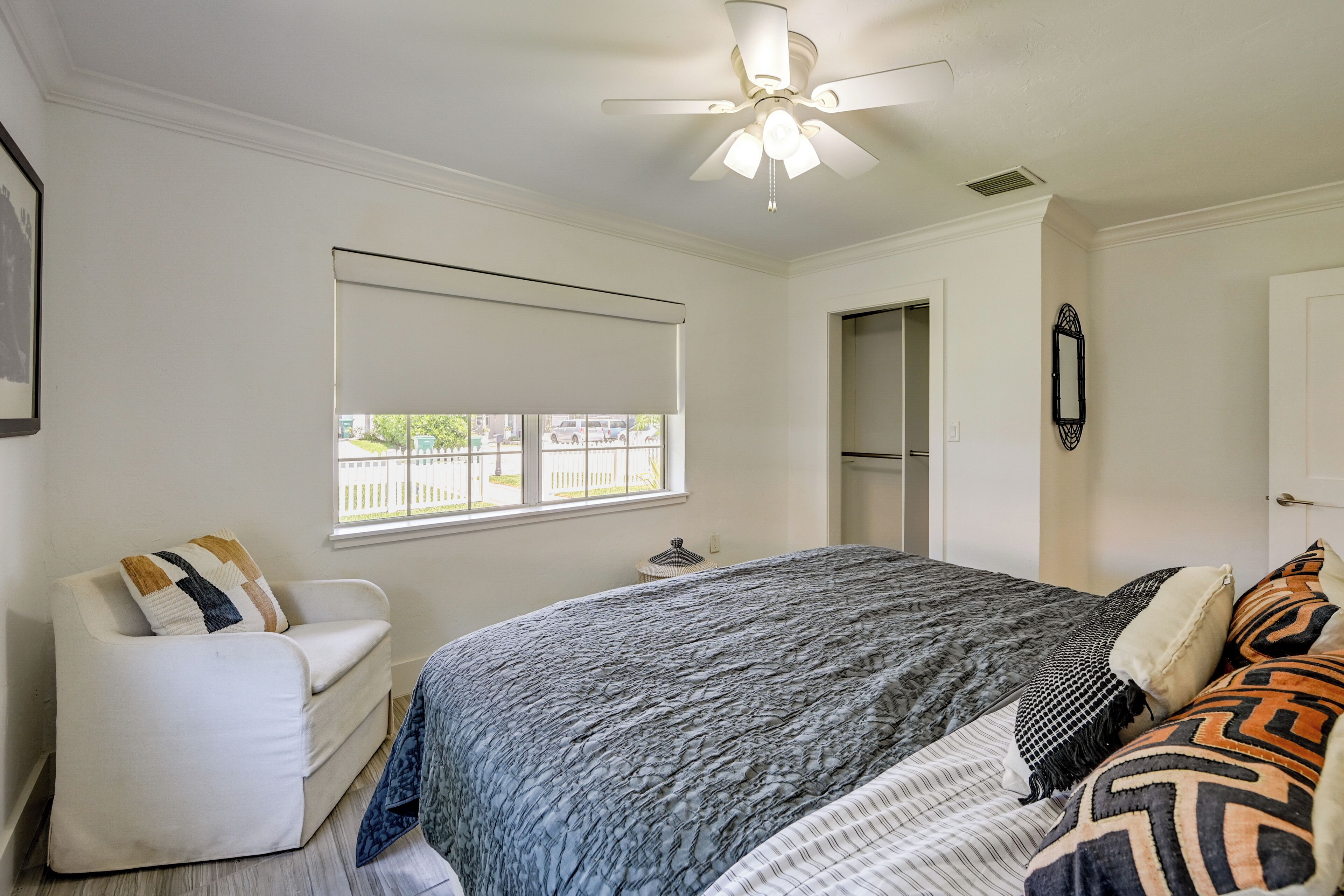 A bedroom with a bed, a chair, a ceiling fan, a window, and a door.