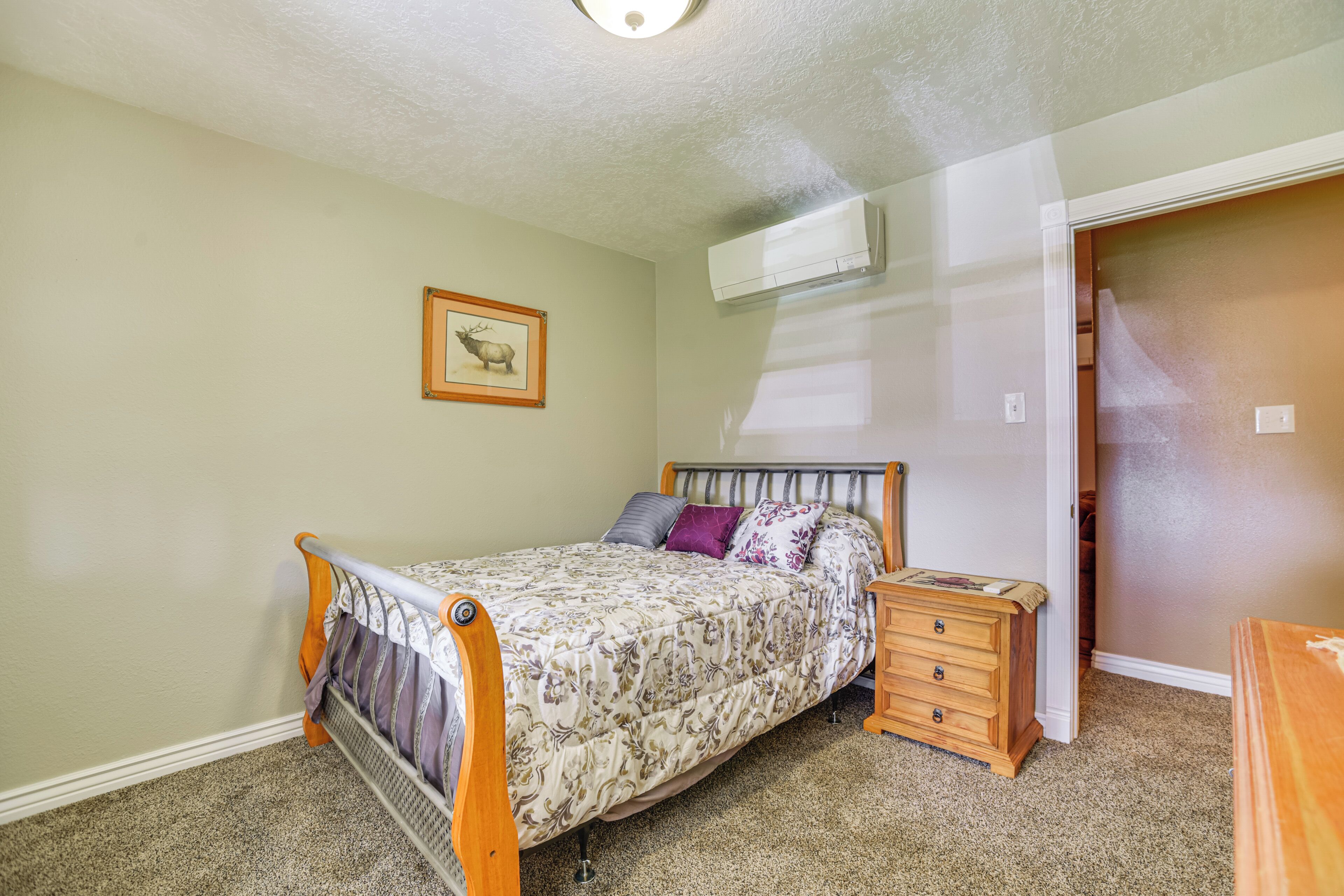 A bedroom with a bed, a nightstand, a dresser, a framed picture on the wall, and an air conditioning unit.