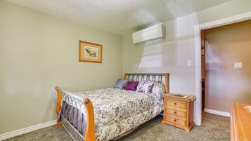 A bedroom with a bed, a nightstand, a dresser, a framed picture on the wall, and an air conditioning unit.