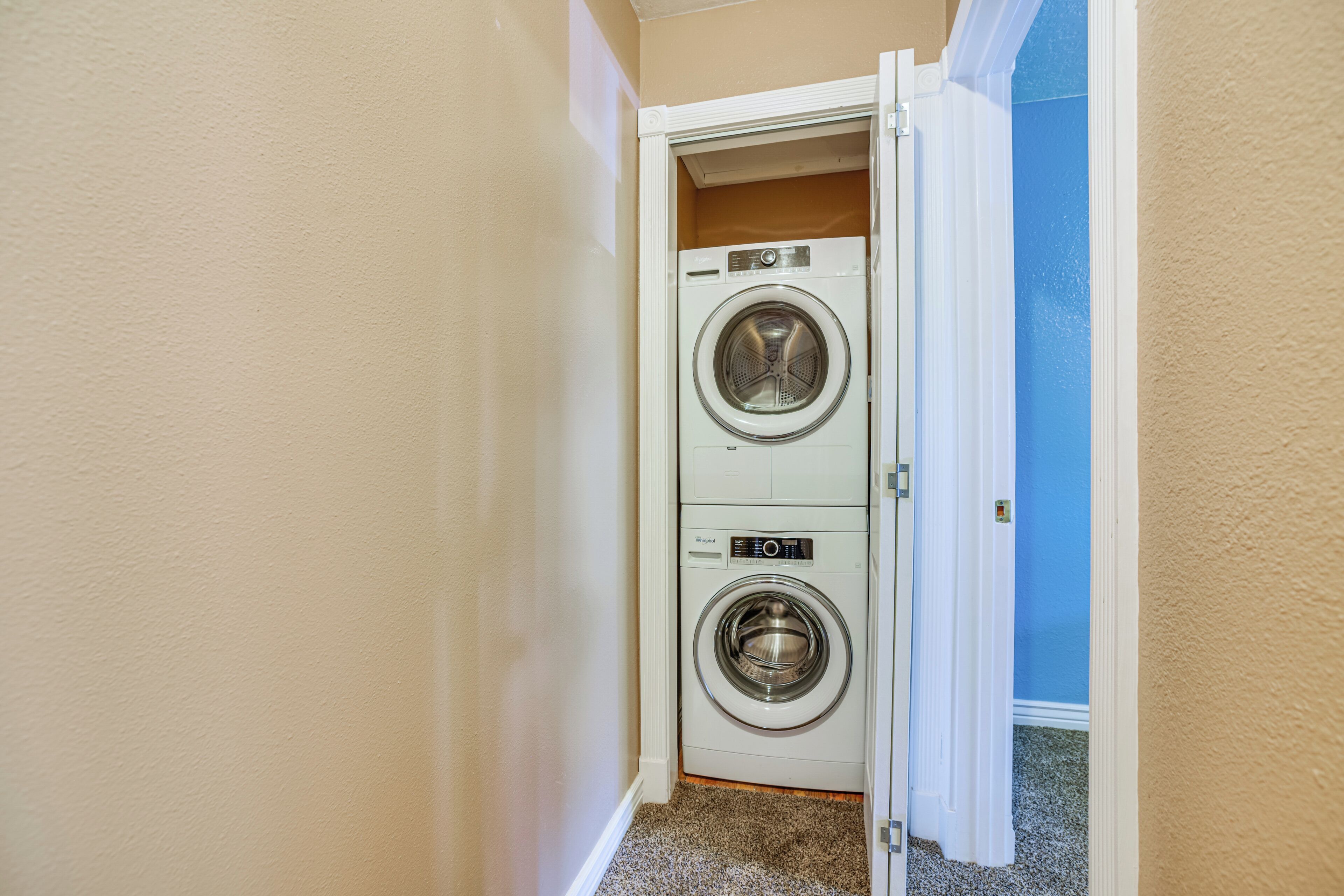 Un cuarto de lavandería con dos lavadoras y secadoras apiladas, paredes color beige y una puerta azul.