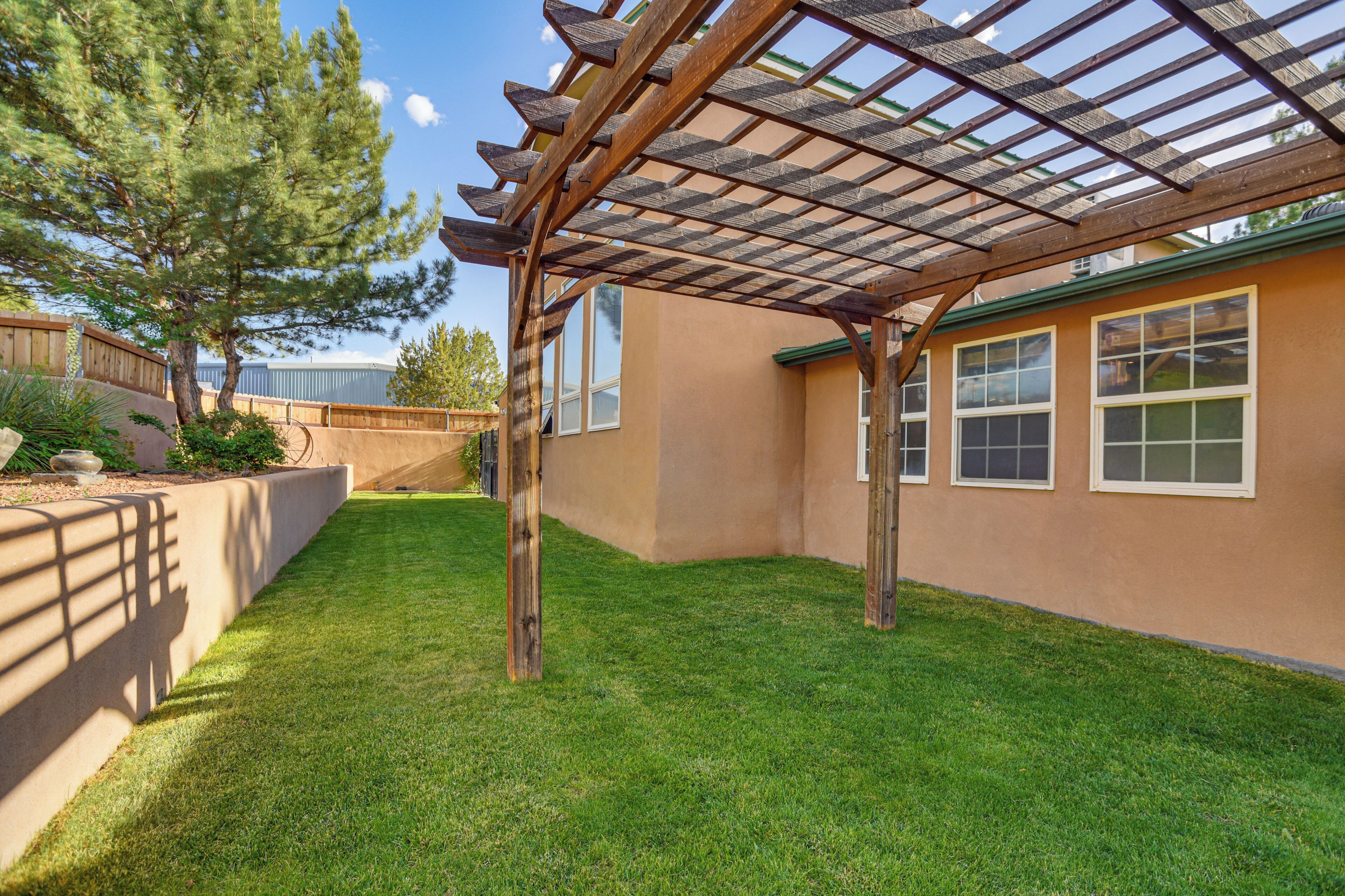 A covered patio area with a pergola, a well-maintained lawn, and a building with windows.