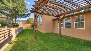 A covered patio area with a pergola, a well-maintained lawn, and a building with windows.