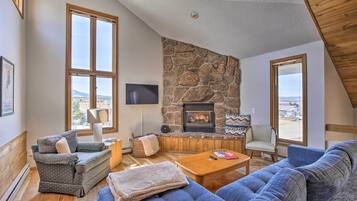 Una sala de estar acogedora con chimenea de piedra, ventanas amplias y un espacio de estar confortable.