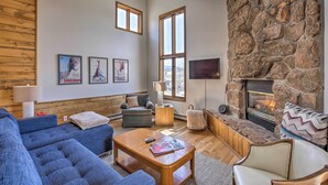 A cozy living room with a stone fireplace, blue sofas, and a flat-screen TV. - Modern Condo w/ Balcony & Bbq, 6 Mi to Winter Park (Fraser)