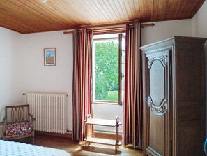 A room with a wooden ceiling, a radiator, a chair, a wooden bench, a wardrobe, and a window with curtains. - Le Village by Interhome (Meuvaines)